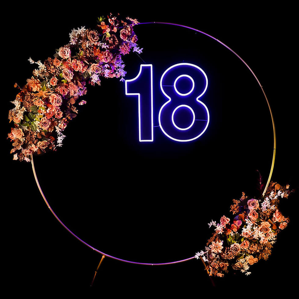 blue 18 neon sign hanging inside gold hoop backdrop with flower arrangement