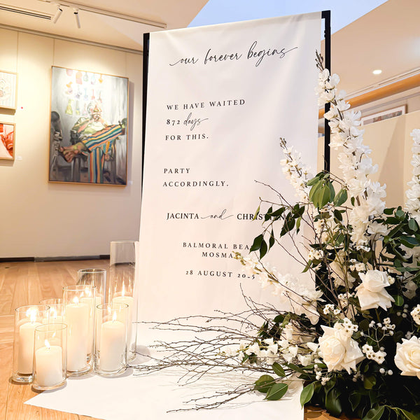 Wedding entrance setup with a decorative linen welcome sign and floral arrangement in an indoor setting.
