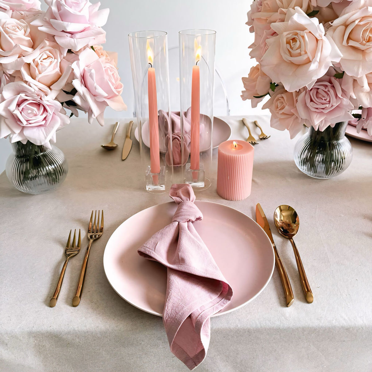 pink napkin and plate on beige tablecloth with rose gold cutlery and pink flower arrangements and candles