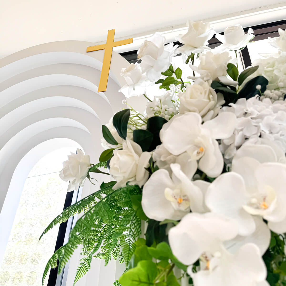 Close up of white and green florals with gold cross on backdrop in background