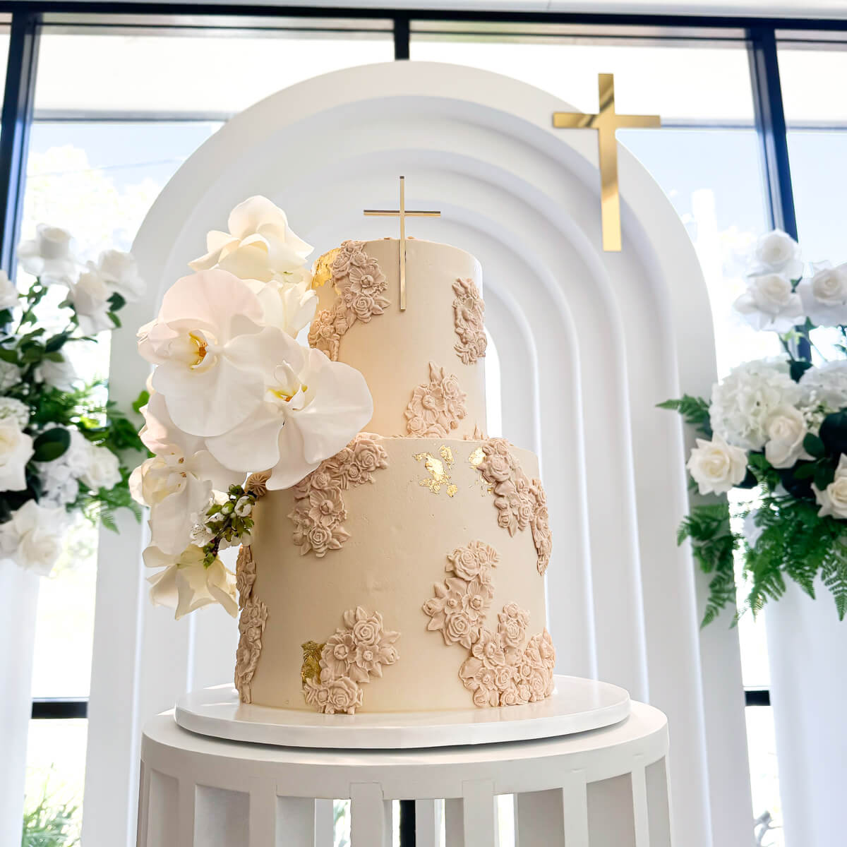 close up of cake on white ripple plinth with white a green florals in background