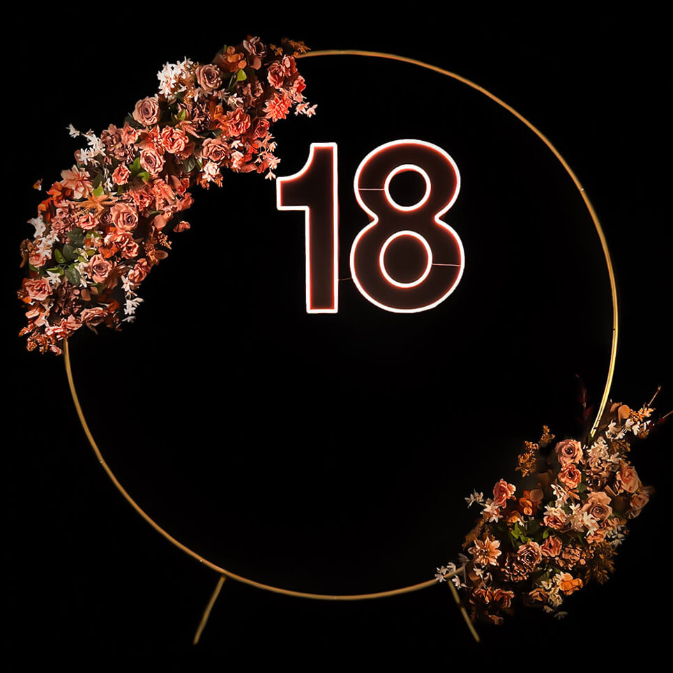 warm white 18 neon sign hanging inside gold hoop backdrop with flower garland