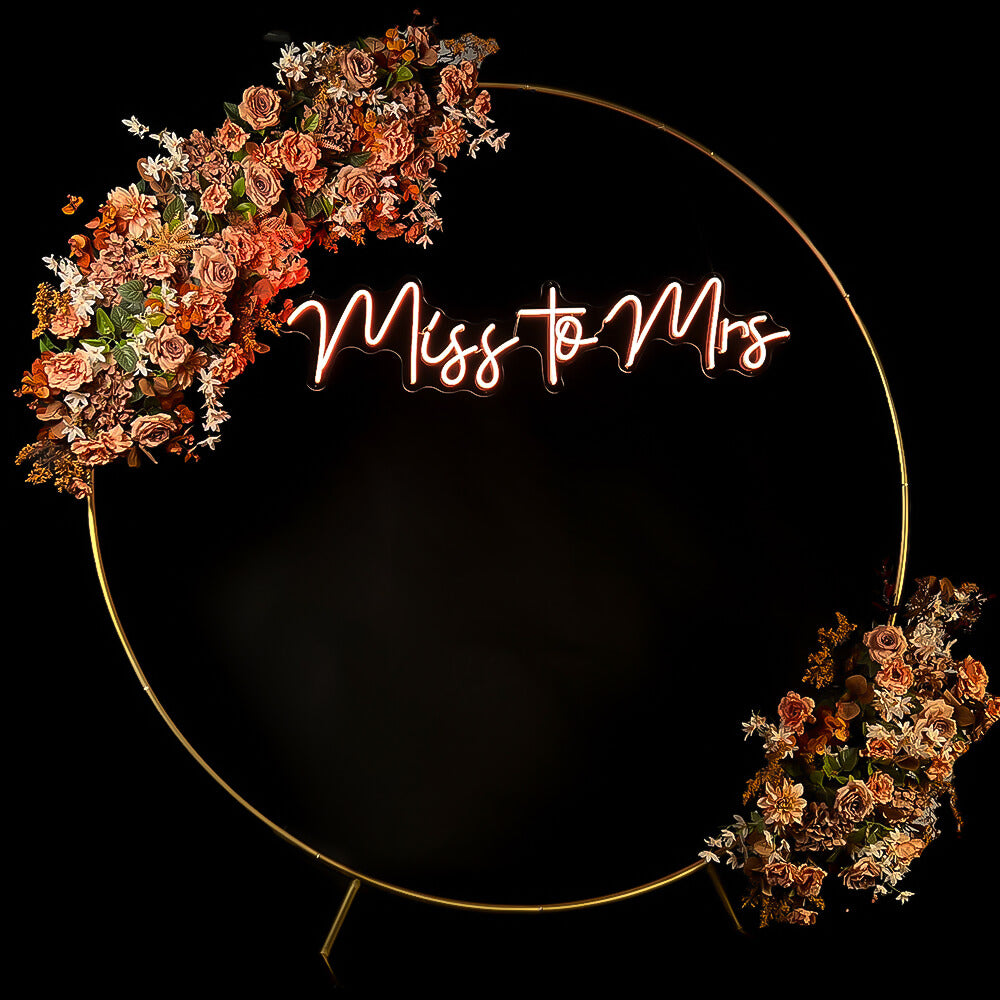 warm white miss to mrs neon sign hanging inside gold circle backdrop with flower garland
