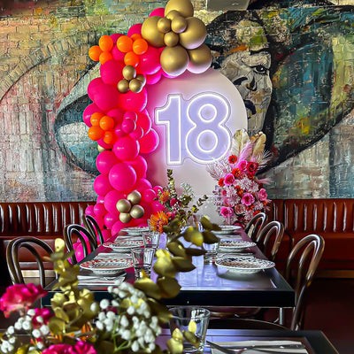 white 18 neon sign on arch backdrop with pink and gold balloon arrangement at restaurant