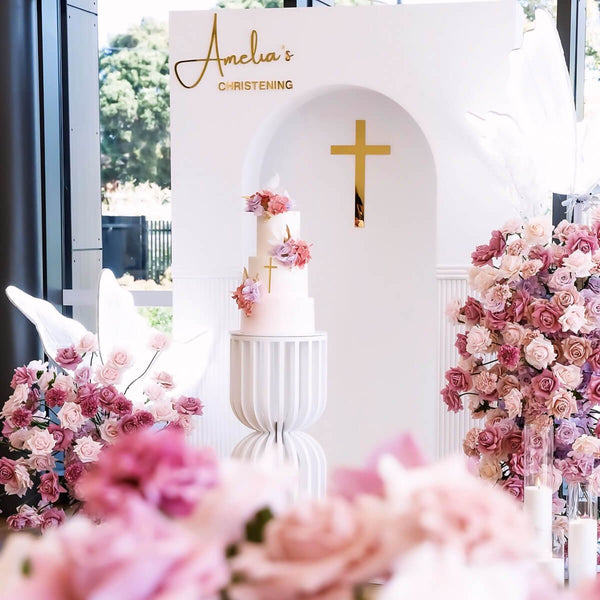 white arch backdrop with crucifix behind mixed pink flower arrangements at christening