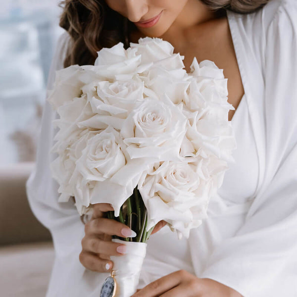 bride looking at and holding bouquet of white roses on wedding day