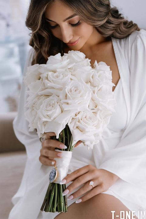 bride looking at and holding bouquet of white roses on wedding day