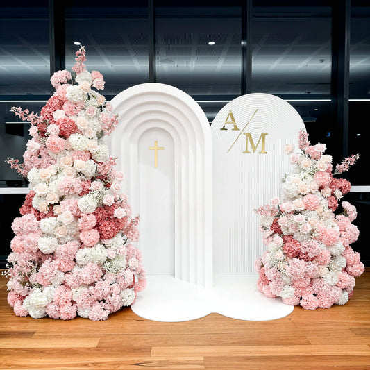 two white arch backdrops on white floor mat with large mixed pink flower towers on outside
