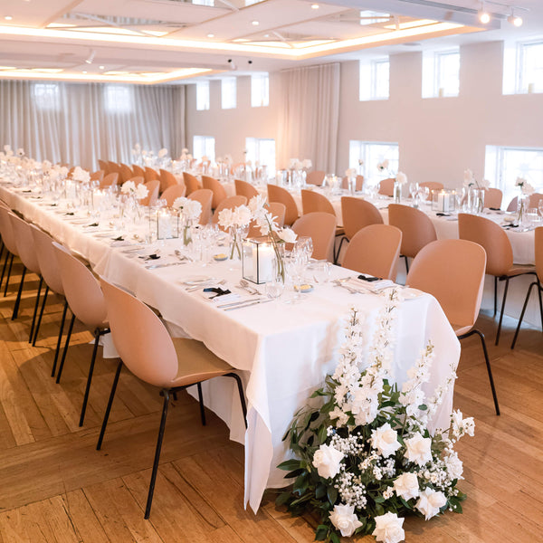 Wedding reception dining room with long tables set for a meal, chairs, and floral centerpieces.
