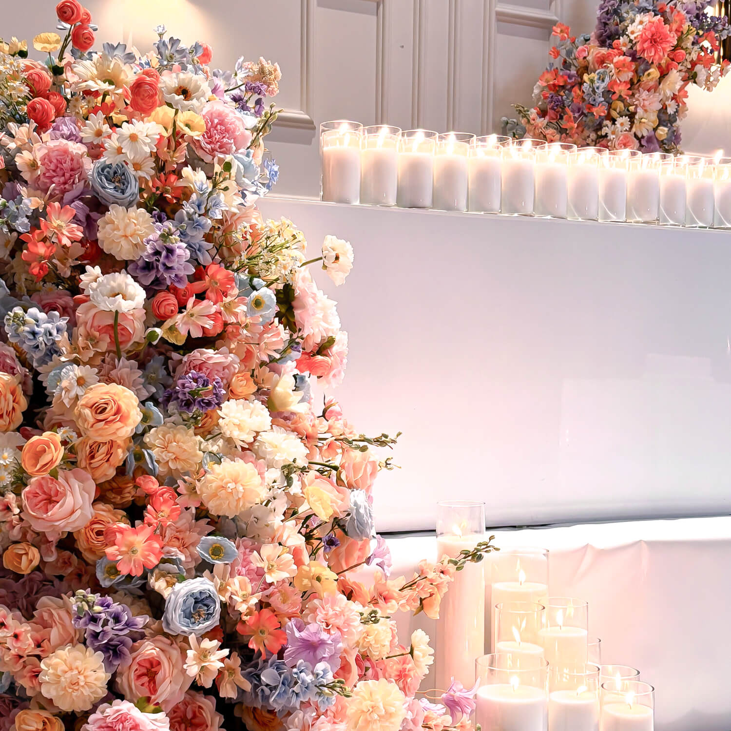 Large spring coloured bridal table floral arrangement with white sand candles on a white acrylic surface