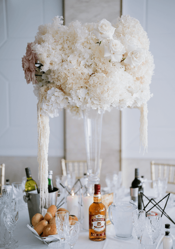 large white and pink flower arrangement on top of tall flute vase on guest table at wedding