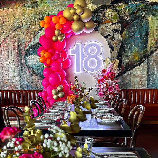 white 18 neon sign hanging on arch backdrop with pink and gold balloon arch and flowers