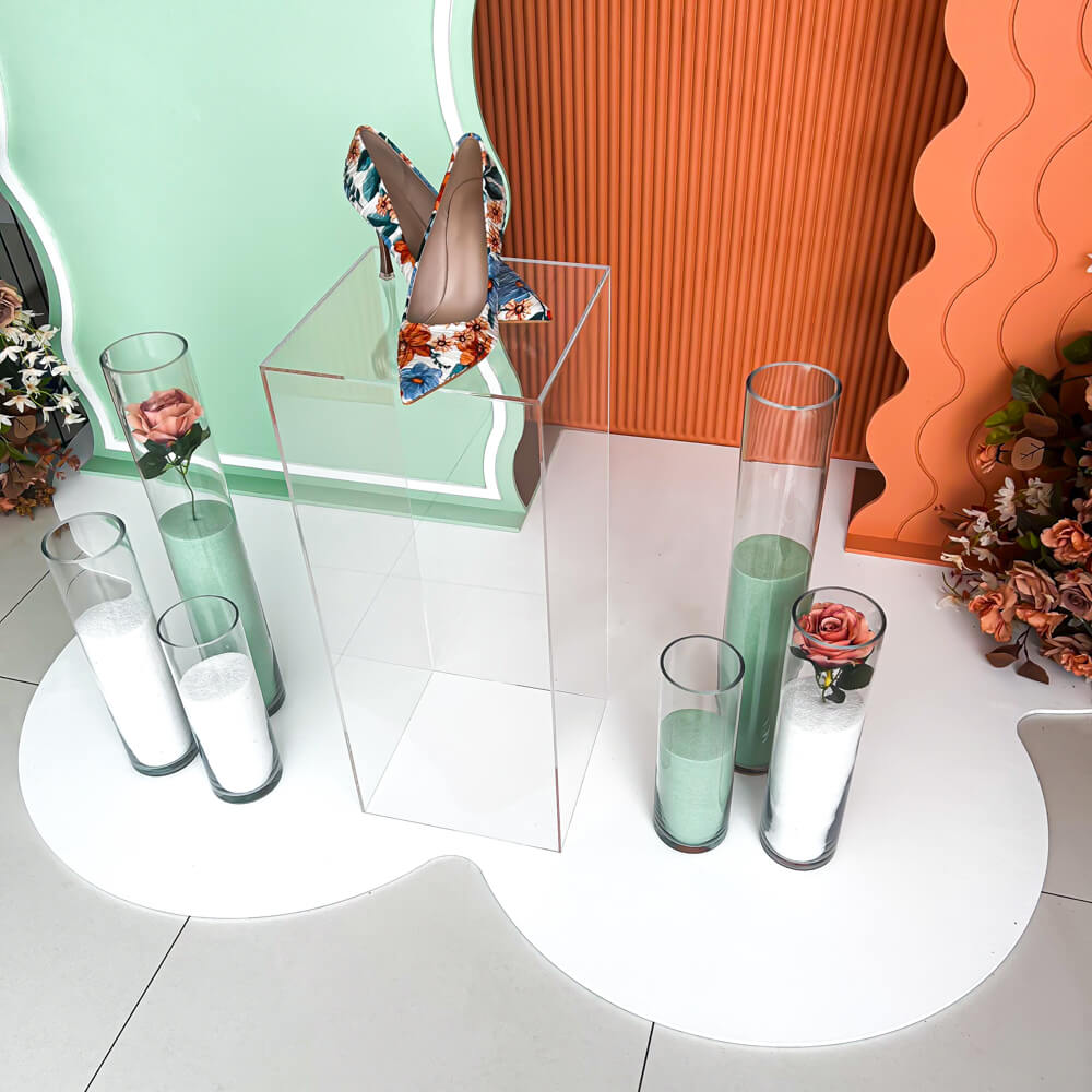 heels placed on clear plinth with sand candles and green and orange backdrops