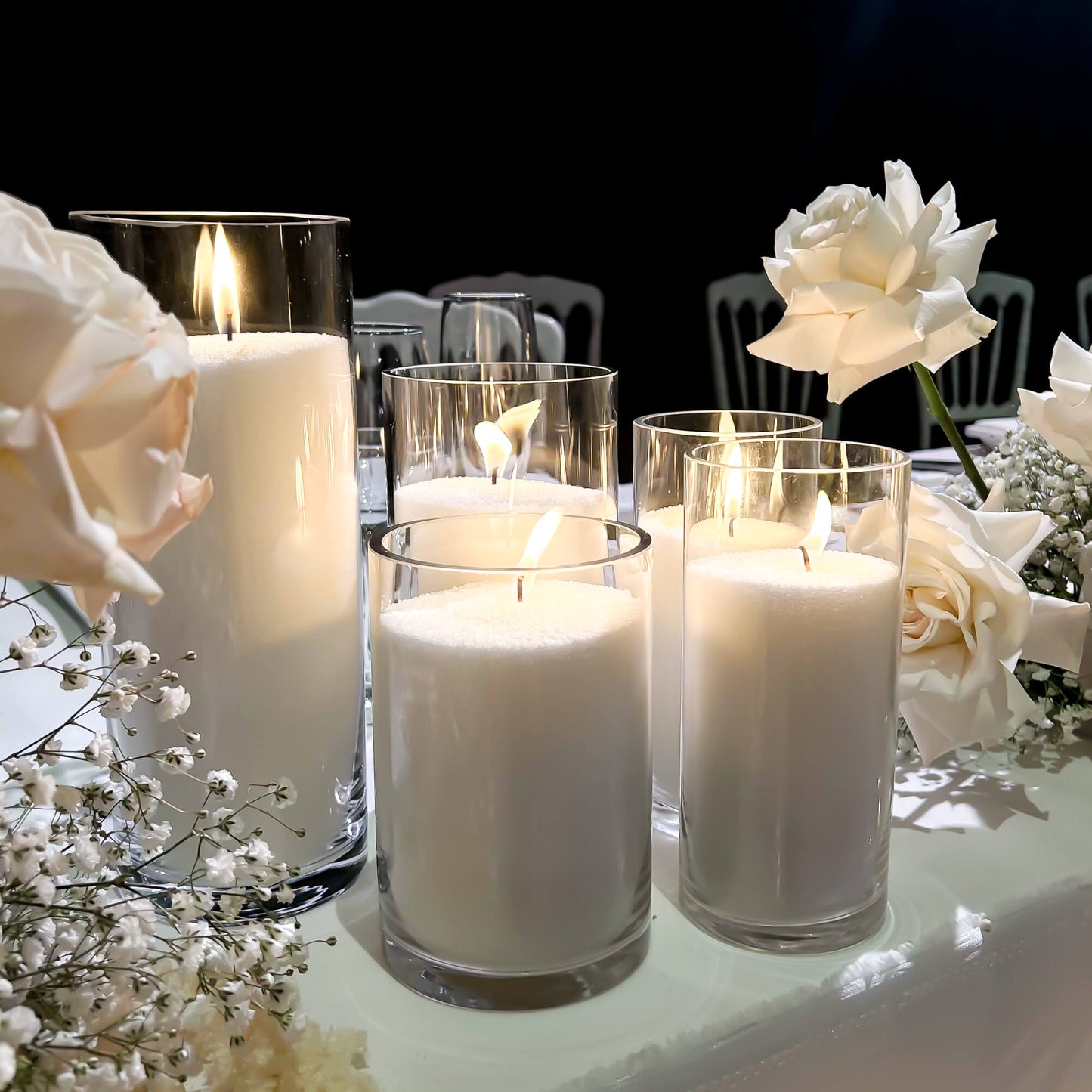 Candlelit setting with white sand candles and flowers on a table.