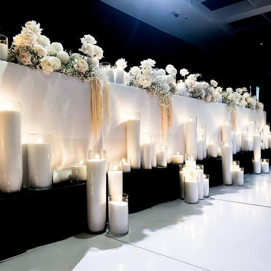 mixed height white sand candles in front of bridal table with flower arrangements on top of bridal table