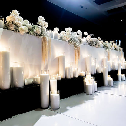 mixed height white sand candles in front of bridal table with flower arrangements on top of bridal table